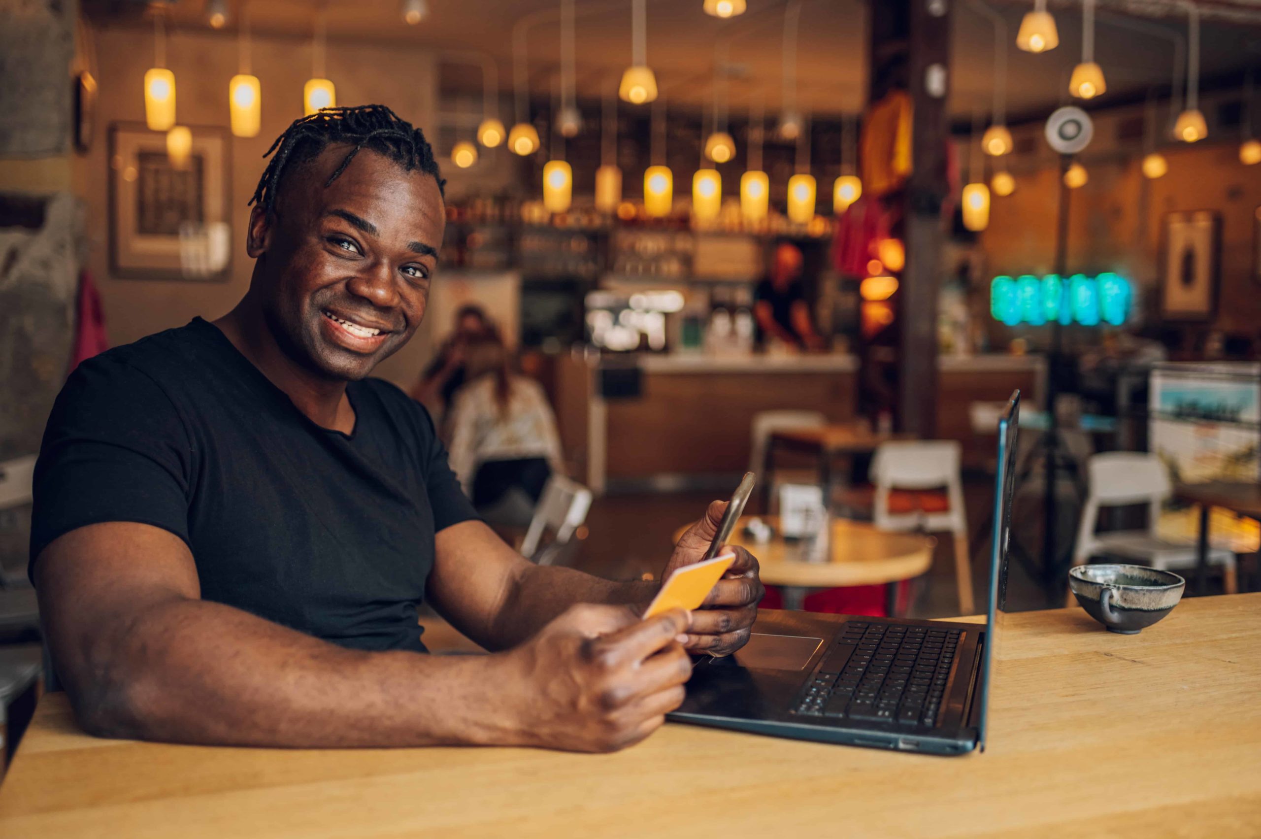 African american man using smartphone and credit card in a cafe