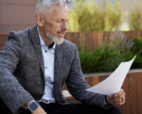 a man in grey blazer sitting on a bench and looking the piece of paper